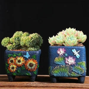 Two blue ceramic succulent planters with embossed sunflowers and lotus flowers on wood