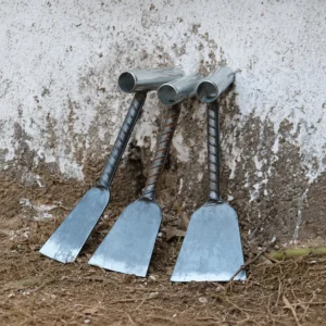 Three hand-forged rebar weeding hoes leaning against a wall