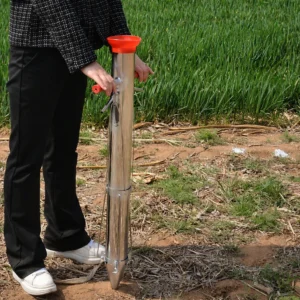 Person using a stainless steel manual seedling transplanter in a field